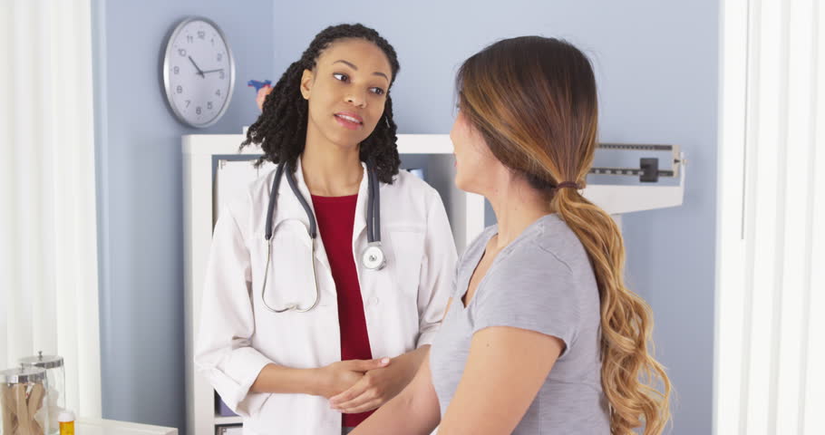 African American Doctor Talking To Female Asian Patient In Exam Room